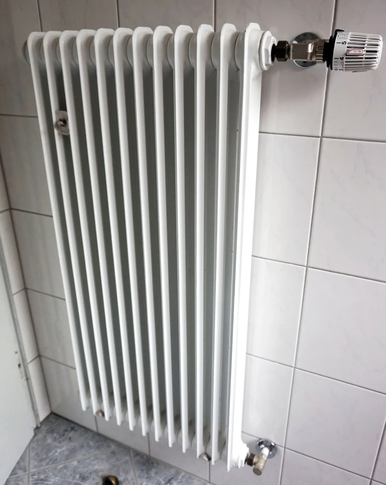 Biały grzejnik żeliwny z pokrętłem termostatu na tle jasnej ściany